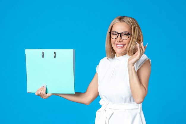 Front view of female worker in white dress holding blue folder on blue wall