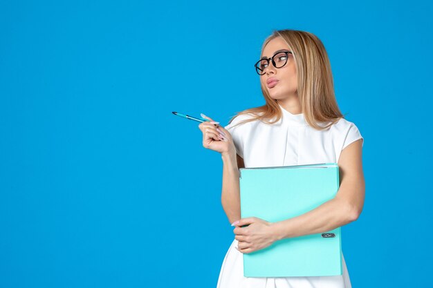 Front view of female worker in white dress holding blue folder on blue wall