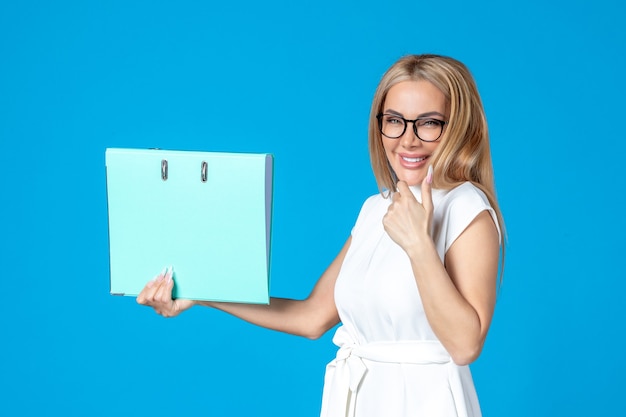 Front view of female worker in white dress holding blue folder on blue wall