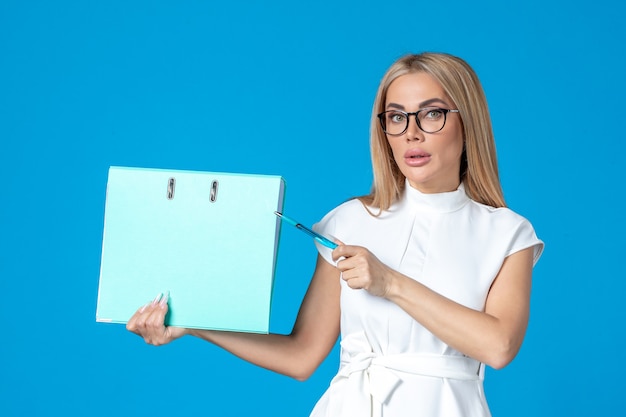 Front view of female worker in white dress holding blue folder on blue wall