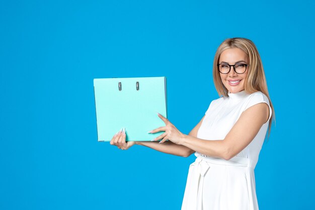Front view of female worker in white dress holding blue folder on blue wall