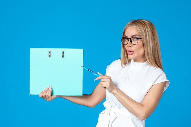 Front view of female worker in white dress holding blue folder on blue wall