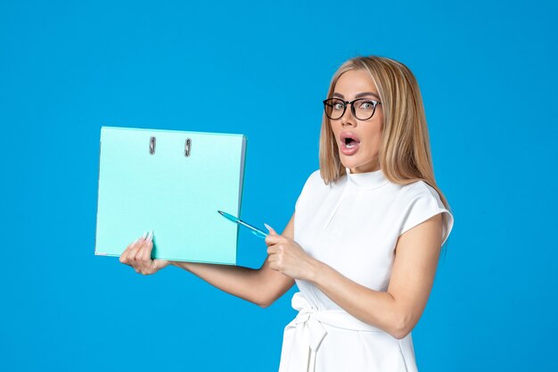 Front view of female worker in white dress holding blue folder on blue wall