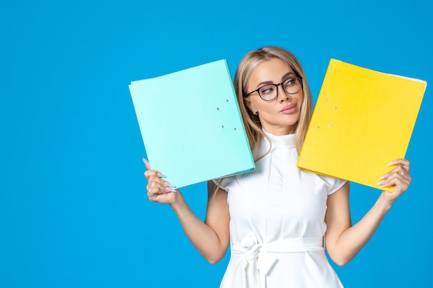 Front view of female worker in white dress holding different folder on blue wall