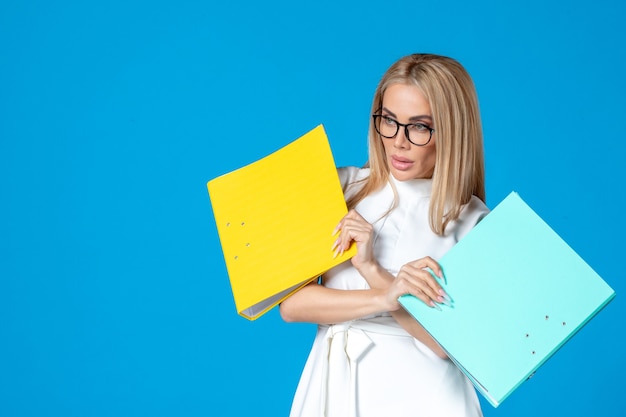 Front view of female worker in white dress holding different folder on blue wall