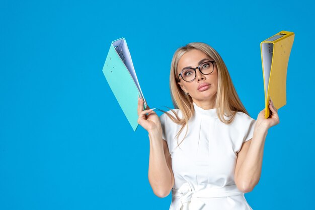 Front view of female worker in white dress holding different folder on blue wall