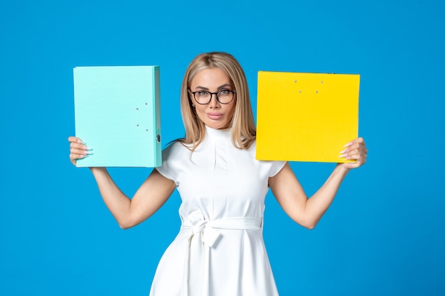 Front view of female worker in white dress holding different folder on blue wall