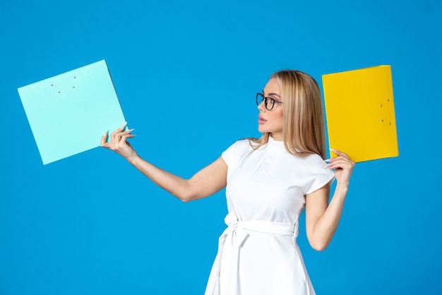 Front view of female worker in white dress holding different folder on blue wall