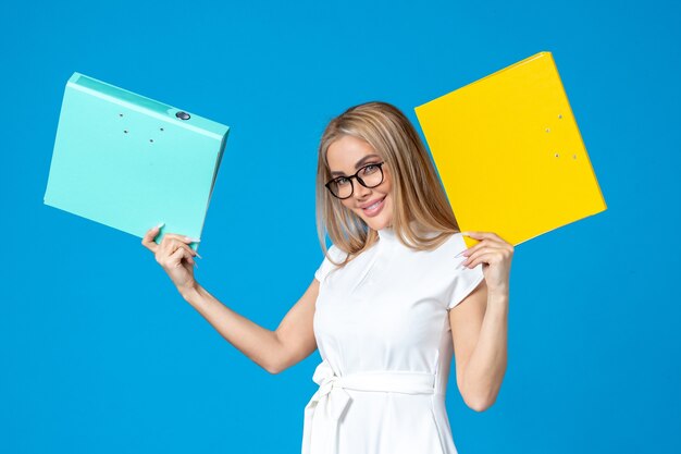 Front view of female worker in white dress holding different folder on blue wall