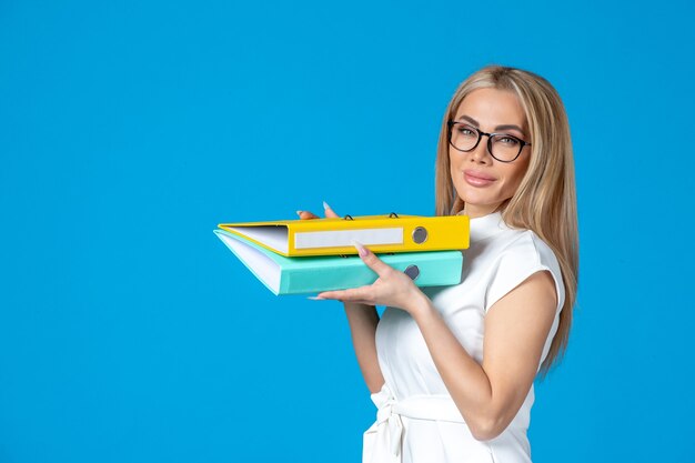 Front view of female worker in white dress holding different folder on blue wall