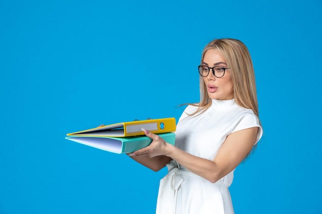 Front view of female worker in white dress holding different folder on blue wall