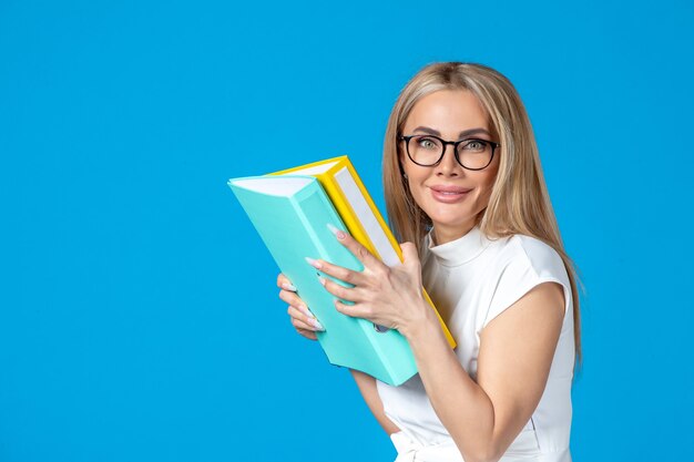 Front view of female worker in white dress holding different folder on blue wall