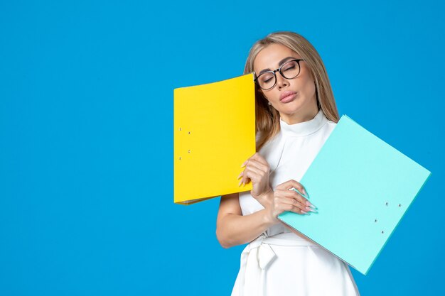 Front view of female worker in white dress holding different folder on blue wall