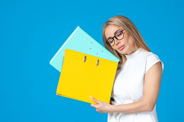 Front view of female worker in white dress holding different folder on blue wall