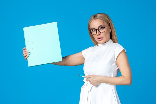 Front view of female worker in white dress holding folder on blue wall