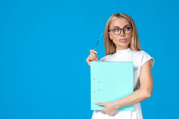 Front view of female worker in white dress holding folder on blue wall