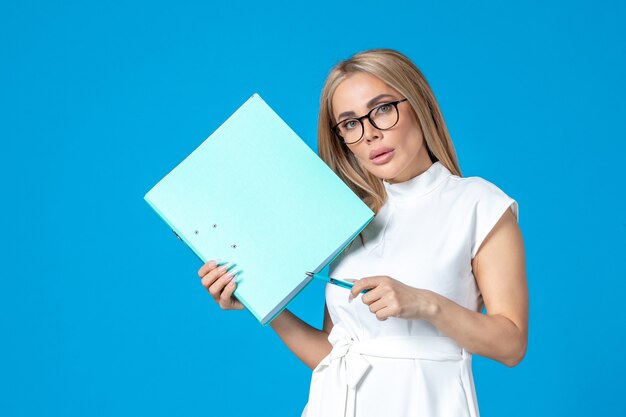 Front view of female worker in white dress holding folder on blue wall