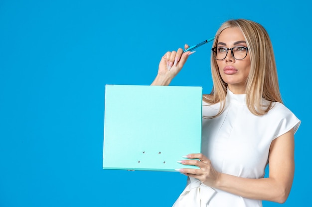 Front view of female worker in white dress holding folder on blue wall