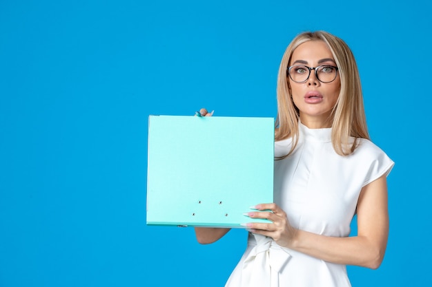 Front view of female worker in white dress holding folder on blue wall