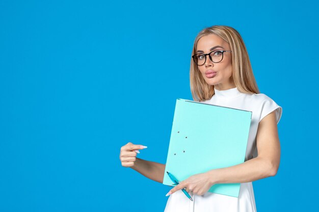 Front view of female worker in white dress holding folder on blue wall