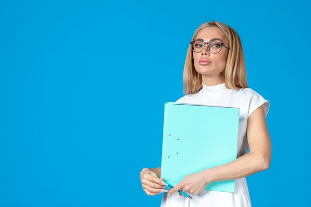 Front view of female worker in white dress holding folder on blue wall