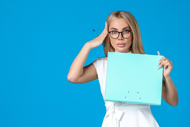 Front view of female worker in white dress holding folder on blue wall