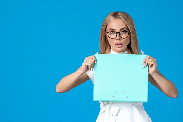 Front view of female worker in white dress holding folder on blue wall