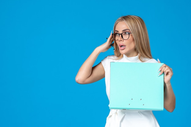 Front view of female worker in white dress holding folder on blue wall