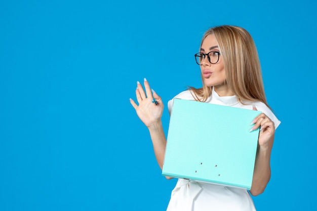 Front view of female worker in white dress holding folder on blue wall