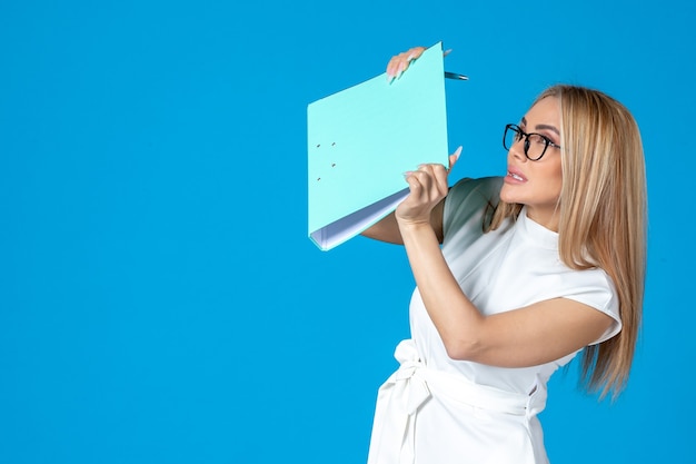 Front view of female worker in white dress holding folder on blue wall