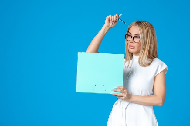 Front view of female worker in white dress holding folder on blue wall