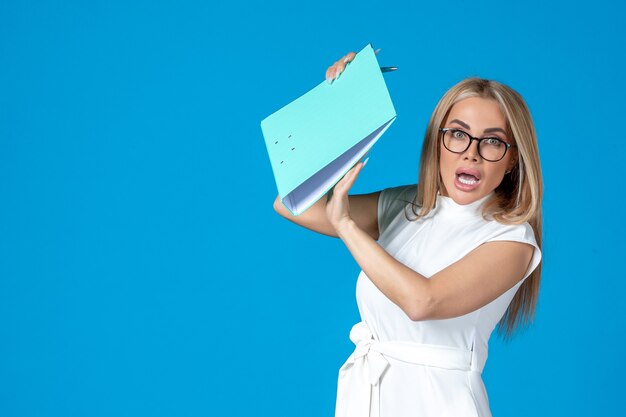 Front view of female worker in white dress holding folder on blue wall