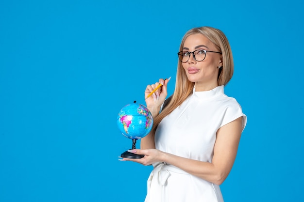 Front view of female worker in white dress holding little earth globe on blue wall