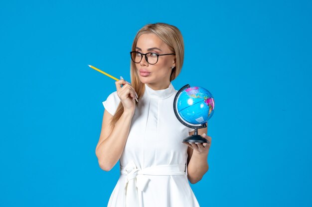 Front view of female worker in white dress holding little earth globe on blue wall