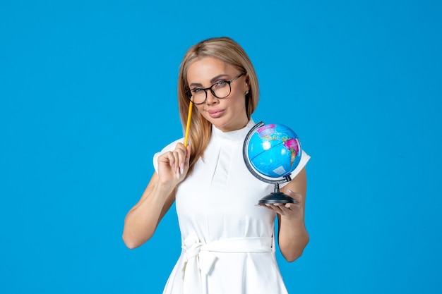 Front view of female worker in white dress holding little earth globe on blue wall