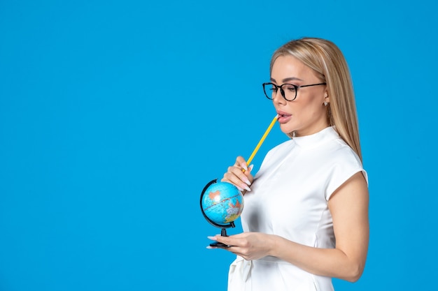 Front view of female worker in white dress holding little earth globe on blue wall