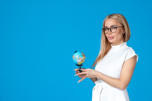 Front view of female worker in white dress holding little earth globe on blue wall