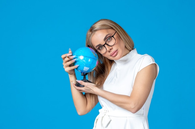 Front view of female worker in white dress holding little earth globe on blue wall