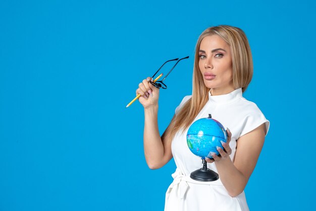 Front view of female worker in white dress holding little earth globe on blue wall