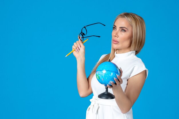 Front view of female worker in white dress holding little earth globe on blue wall