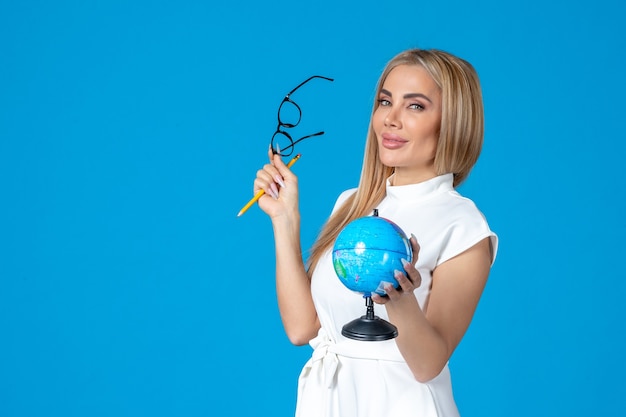 Front view of female worker in white dress holding little earth globe on blue wall