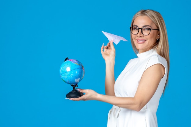 Free photo front view of female worker in white dress holding little earth globe on blue wall