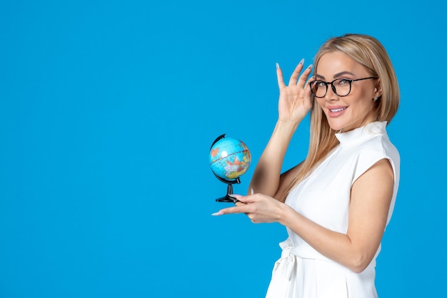 Front view of female worker in white dress holding little earth globe on blue wall