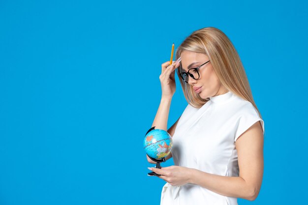 Front view of female worker in white dress holding little earth globe on blue wall