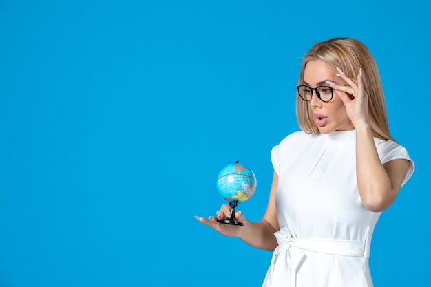 Front view of female worker in white dress holding little earth globe on blue wall