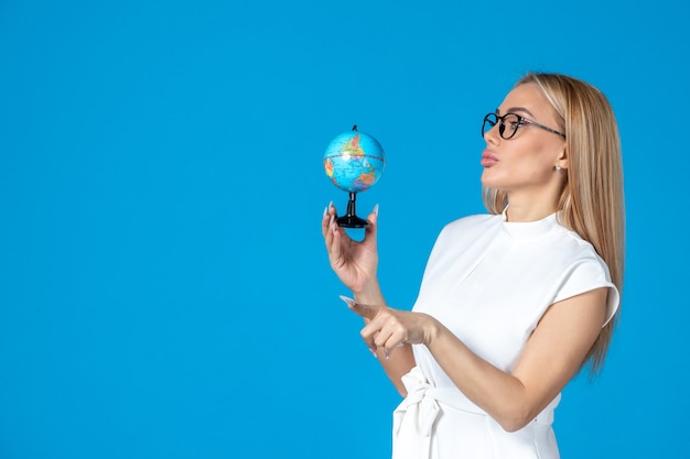 Front view of female worker in white dress holding little earth globe on blue wall