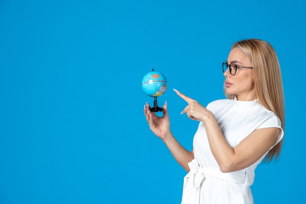 Free photo front view of female worker in white dress holding little earth globe on blue wall