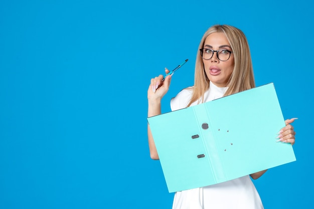 Front view of female worker in white dress holding open folder on blue wall