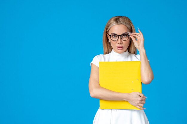 Front view of female worker in white dress holding yellow folder on blue wall