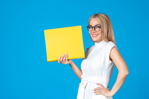 Front view of female worker in white dress holding yellow folder on blue wall